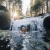 A woman wearing a hat and swimsuit smiles as she dries herself with an orange towel after a cold bath in the winter forest.