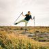 Elliot Dickinson balances laughing in a CRIVIT hiking outfit with two trekking poles on a rock in an autumnal heath landscape