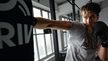 Muž v boxerských rukavicích CRIVIT udeřuje do boxovacího pytle v posilovně