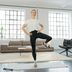 CRIVIT Fitness-Expertin Linda steht in einem hellen Wohnzimmer in einer Balance‑Übung auf einem Bein.