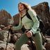 Femme en veste outdoor et legging CRIVIT randonnant sur terrain rocheux avec bâtons de marche
