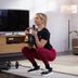 CRIVIT-fitnessexpert Linda doet een oefening met een kettlebell in een woonkamer, gehurkt op een mat en met halters op de achtergrond.