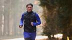 Hardloopexpert Tim gaat joggen in het bos, gekleed in een zwart CRIVIT-functioneel herenvest en een blauw functioneel shirt.