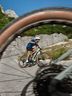 Man in CRIVIT cycling gear riding an e-mountain bike on a rocky alpine road framed by a wheel