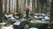 Woman in CRIVIT sports outfit meditates on rocks by a winter stream in a snowy forest.
