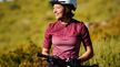 Mujer en la naturaleza, sentada en una bicicleta y llevando ropa deportiva y un casco de bicicleta.