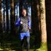 Gemotiveerde expert Tim jogt door een bos in zwarte en blauwe CRIVIT-hardloopkleding.