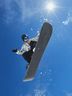 Man in CRIVIT snowboard jacket performing a high jump against a blue sky