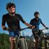 Zwei Männer in CRIVIT-Radfahrausrüstung fahren Mountainbikes auf einer Alpenstraße