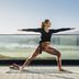 Woman in CRIVIT yoga outfit performing Warrior II pose on a terrace with mountain panorama.