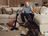 Andre Agassi sitting on a sofa, reacting playfully as a large dog sits amid torn stuffing on the carpet, with a cordless SILVERCREST vacuum cleaner nearby in a cozy living room.