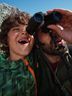 A man and a child wearing CRIVIT sportswear look through binoculars against a mountain backdrop