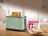 SILVERCREST Doppelschlitz-Toaster STC 850 E4 in zartem Mintgrün auf einer Holzarbeitsplatte. Zwei goldbraun geröstete Toastscheiben und ein Marmeladenglas im Hintergrund.