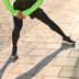 L'expert Tim fait un étirement de l'intérieur de la cuisse pendant la phase de récupération sur un sol pavé, en collant de course CRIVIT noir et t-shirt fonctionnel vert fluo.