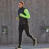 L'expert Tim, portant un gilet fonctionnel noir pour homme par-dessus un t-shirt fonctionnel vert fluo, fait un jogging décontracté dans une cour.
