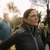 Woman in a CRIVIT vest stretches outdoors with a group of runners in a sunny park.