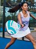 A woman wearing a CRIVIT performance top and functional skort, playing padel with a white padel racket on an outdoor court, showcasing dynamic movement.