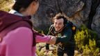 Man reaching out a helping hand to partner while hiking rocky trail wearing CRIVIT softshell jacket and backpack.