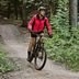 Femme en veste de cyclisme rose CRIVIT roulant en VTT sur un sentier forestier