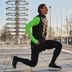 L'expert Tim fait un exercice de mobilisation en plein air, vêtu d'un gilet fonctionnel CRIVIT noir pour homme par-dessus un t-shirt fonctionnel vert fluo.