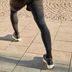 Gros plan sur les jambes et les chaussures de course pendant un étirement des mollets lors de la phase de récupération, avec une tenue de course CRIVIT sur un chemin pavé.