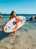 A woman is walking into water bringing her SUP with her.