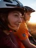 A woman and a man in the picture watching the sunset while wearing a bicycle helmet